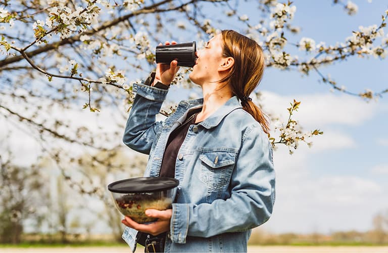 ORNAMIN-Zero-Waste-Coffee-to-go-Mehrwegbecher Frau trinkt unterwegs aus ORNAMIN Coffee to go Mehrwegbecher