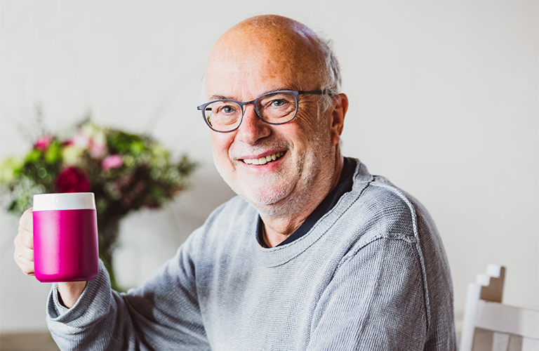 Ein älterer Herr hält eine Tasse mit Kipp-Trick. An elderly gentleman holds a mug with special features.
