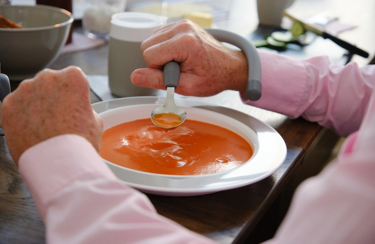 Eine Person isst aus einem Teller mit Kipp-Trick.A person eats from a plate with special features.