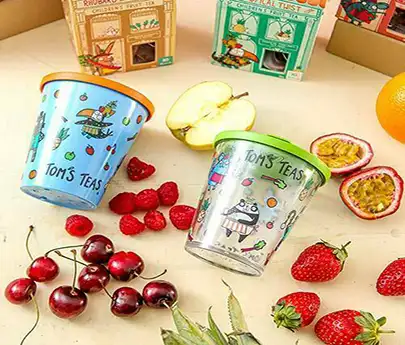 ORNAMIN-Kinder-Mehrwegbecher im Tom's Tea Design Bunt dekorierte to go-Kinderbecher im Toms Tea Design liegen auf einem Tisch