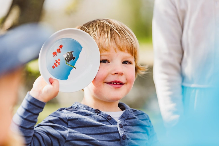 Kind hält Kinderteller hoch. Child holds up child's plate