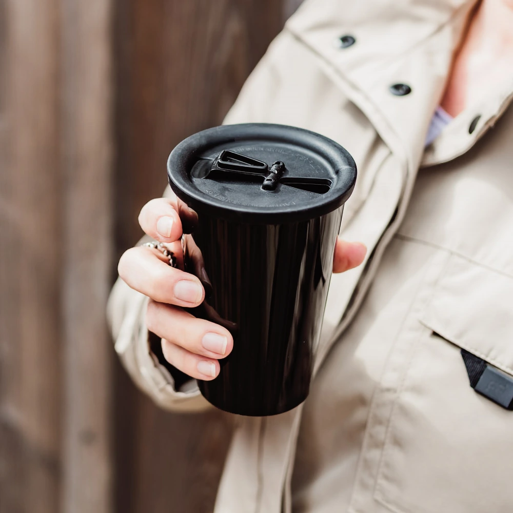 ORNAMIN-to go-Becher für den Kaffee zum Mitnehmen Ein verschlossener Coffee to go Becher in der Hand einer Person