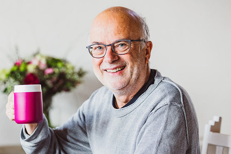 Ein Mann hält einen Becher mit Trink-Trick. A man holds a mug with special feature.