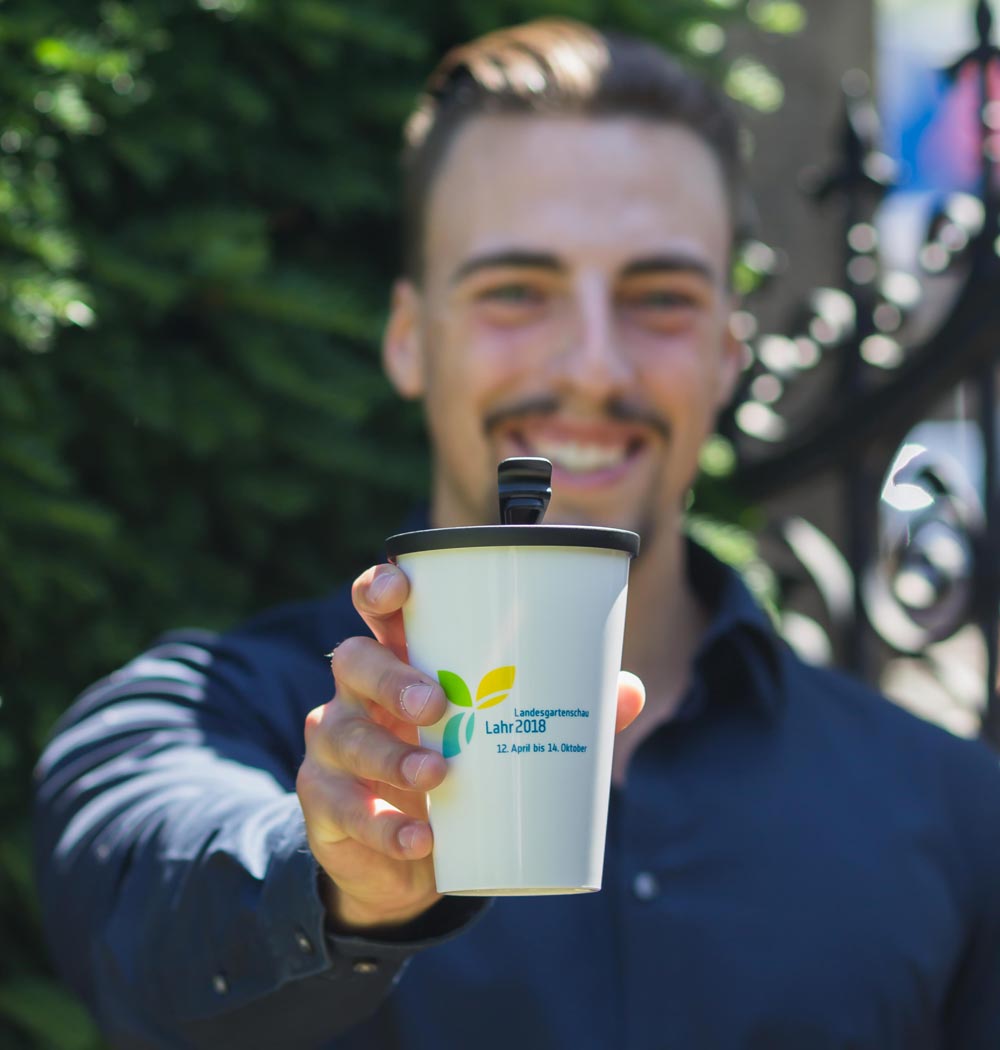 ORNAMIN-Coffee-to-go-Mehrwegbecher-Referenz-Landesgartenschau-Lahr ORNAMIN Coffee to-go Mehrwegbecher im Design der Landesgartenschau Lahr wird in einer Hand gehalten