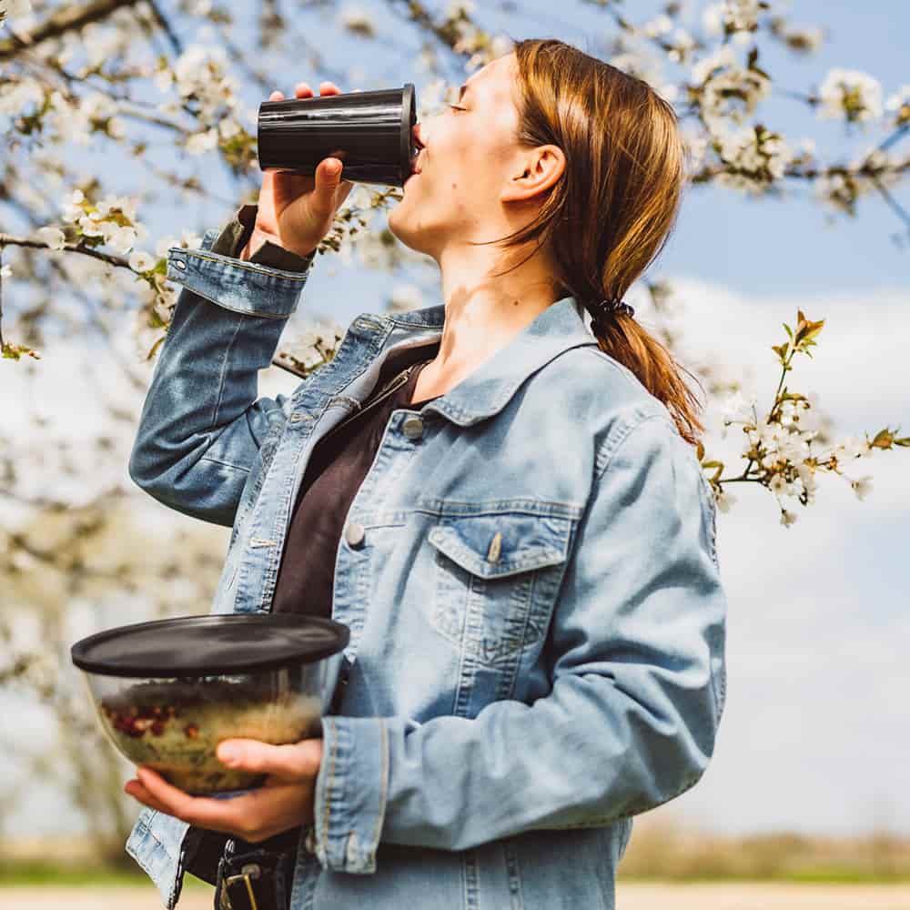 Junge lächelnde Frau trinkt aus einem Mehrwegbecher von ORNAMIN