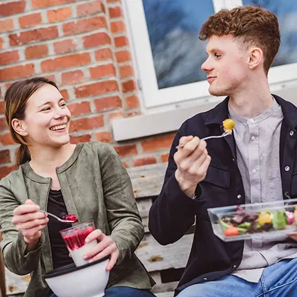 ORNAMIN-Food-to-go-Mehrwegschalen-unterwegs Pärchen guckt sich lächeln an und isst aus Mehrwegschalen von ORNAMIN