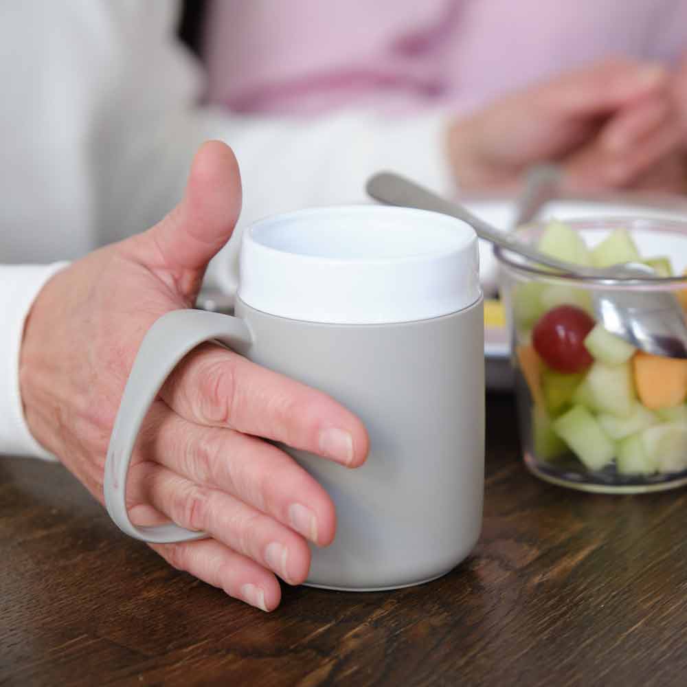 Ornamin-Trinkhilfen-Becher-mit-Trink-Trick ein grauer Ornamin Becher mit Trink Trick wird von einer Hand gehalten