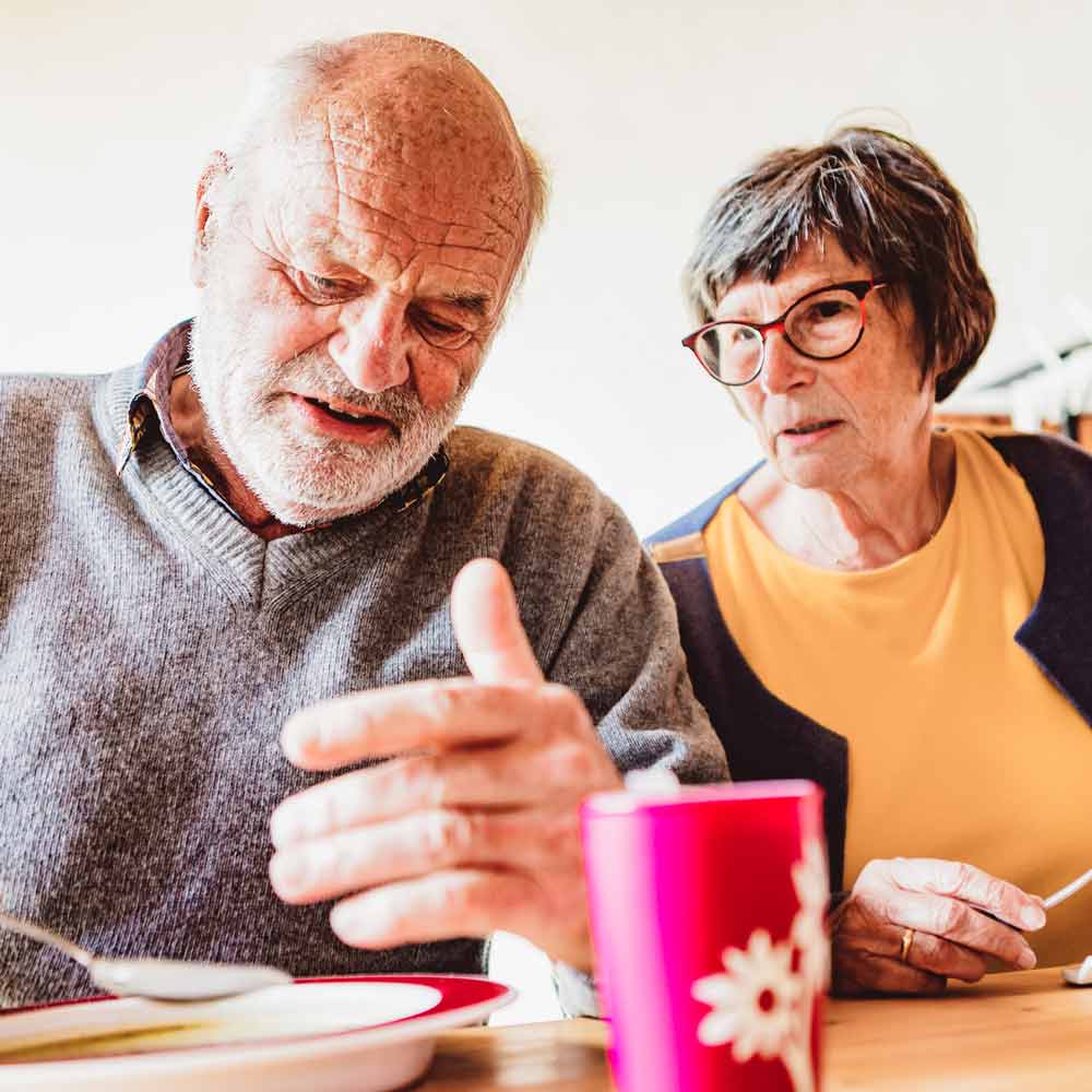Älterer Mann und ältere Frau sitzen am Tisch nebeneinander