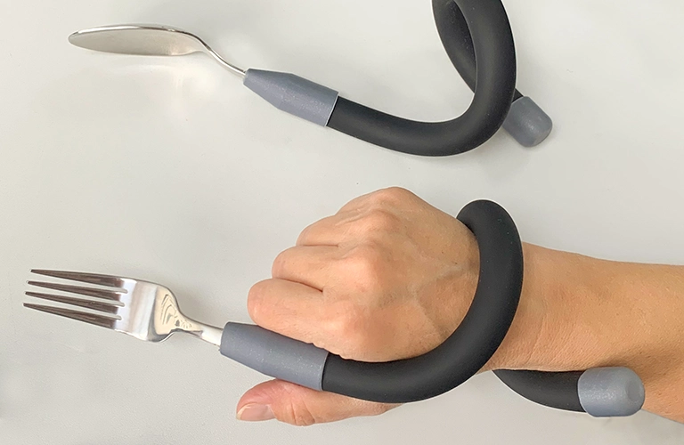 Hand hält eine Gabel mit  biegsamem verlängertem Griff. hand holds a fork with a flexible extended handle.