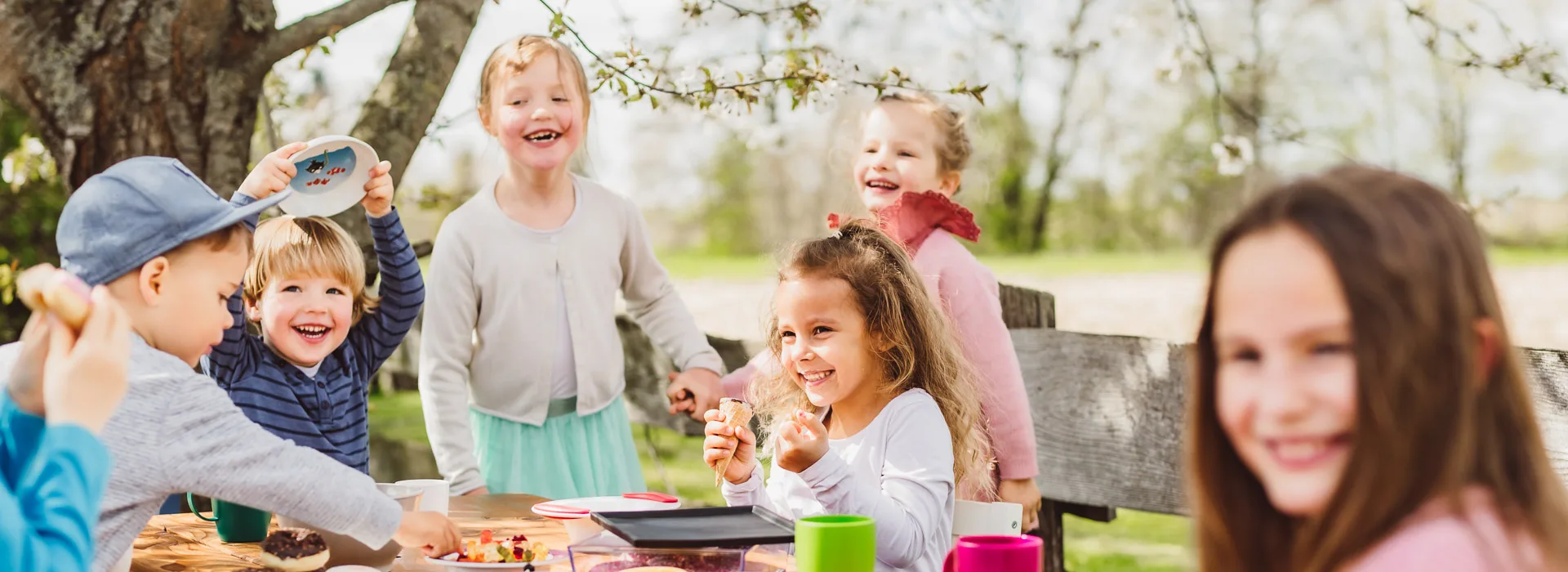 ORNAMIN-Geschirr-Kindergeschirr-Header Gut gelaunte Kinder sitzen draußen unter einem blühendem Baum