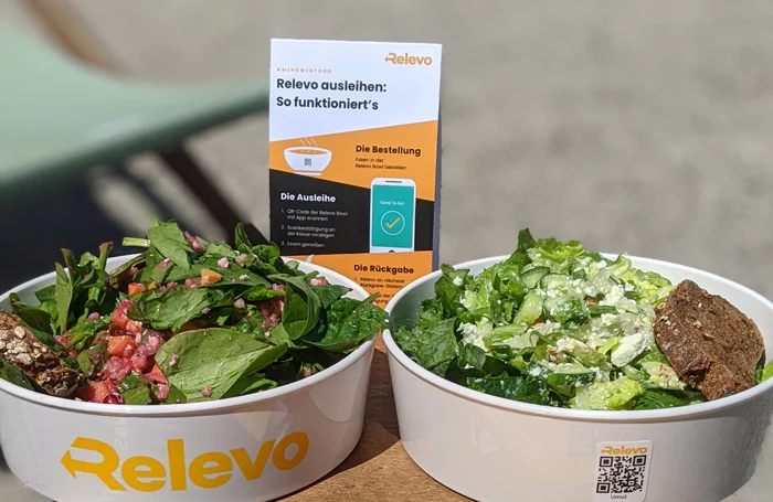 Zwei Schalen mit dem Relevo-Mehrwegsystem- Logo stehen befüllt mit Take away Gerichten draußen auf einem Tisch