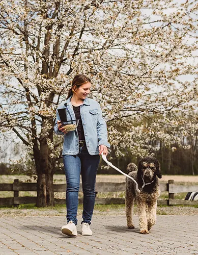 Eine junge Frau ist unterwegs mit ihrem Pudel. Sie hat ihr Mittagessen in Mehrwegschalen dabei.