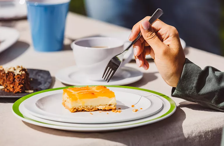 Eine Frau isst im Freien ein Stück Kuchen von einem hochwertigen Kunststoffteller