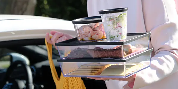 Eine Frau trägt ihren Einkauf an der Frischetheke in einem Stapel Mehrwegschalen