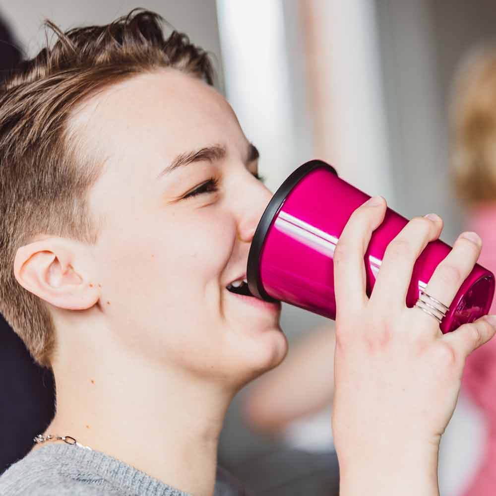 ORNAMIN-Coffee-to-go-Mehrwegbecher Junge lächelnde Frau trinkt aus einem Mehrwegbecher von ORNAMIN