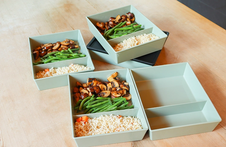ORNAMIN-Mitnehmen - Meal Prep-Set für das Essen zum Mitnehmen Auf dem Tisch stehen fünf Mehrwegboxen mit vorbereitetem Essen für die Mittagspause.