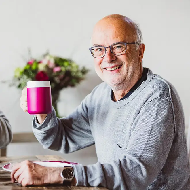 ORNAMIN-Pflegegeschirr-mit-Trick-für-die-häusliche-Pflege Pflegebedürftige-Person-trinkt-selbstständig-mit-dem-ORNAMIN-Becher-mit-Trink-Trick