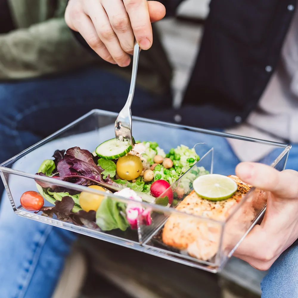 Eine Box ist mit Essen gefüllt und wird von einer Person in der Hand gehalten während sie daraus isst