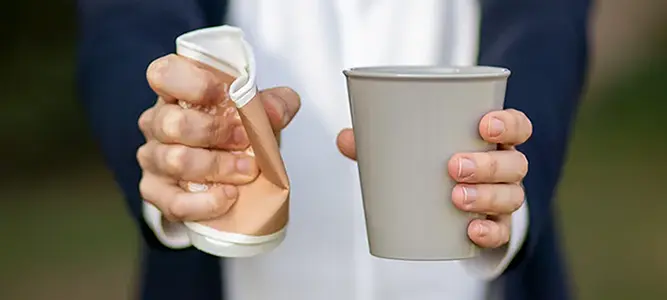 Eine Frau zerdrückt mit ihrer rechten Hand einen Einweg-Becher, in der linken Hand hält sie einen Mehrwegbecher.