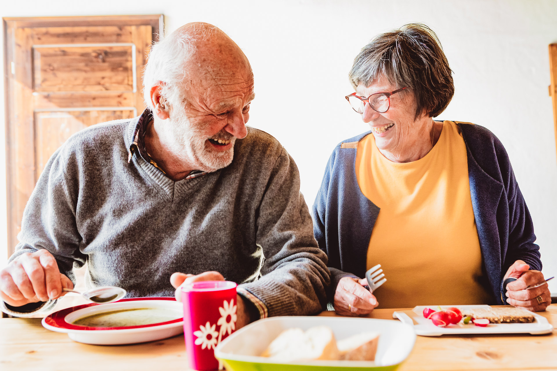 Zwei alte Menschen benutzen am Esstisch Pflegegeschirr 