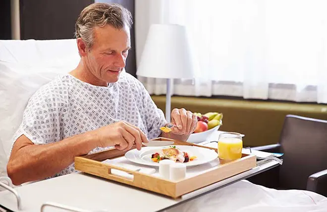 Mann im Krankenbett isst von einem Tablett mit professionellem Pflegegeschirr 