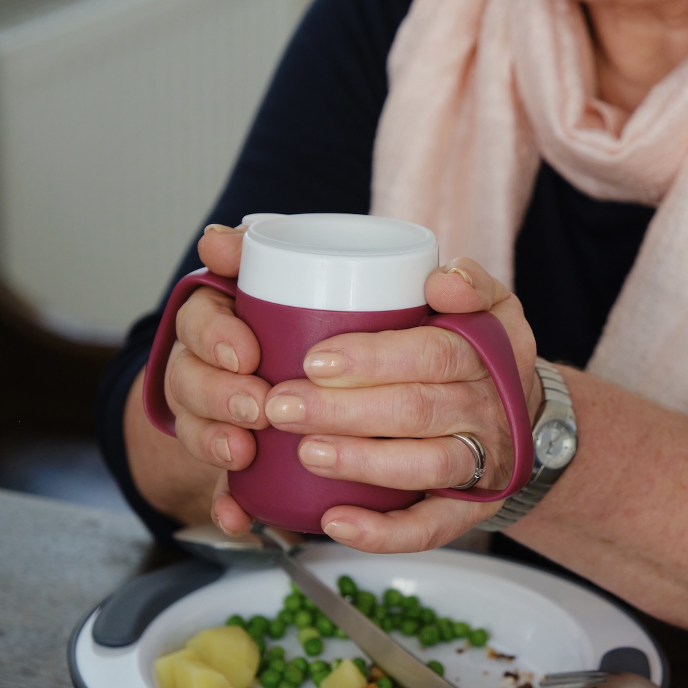 Zwei Hände halten einen Becher mit Trink-Trick. Two hands hold a cup with special drinking features.